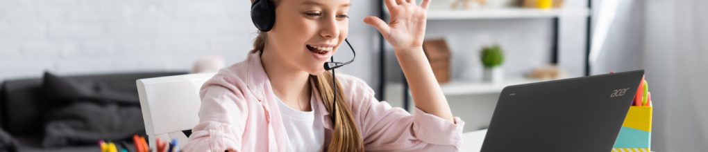 Selective focus of positive kid in headset waving hand during webinar at home